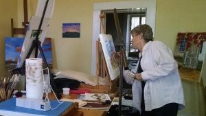Photo of artist Beth Francell working on a pastel on an easel in her studio.